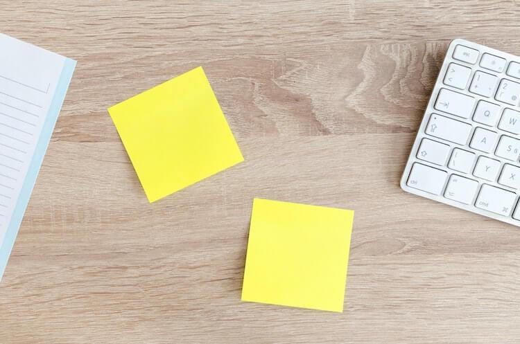 Two yellow post-it notes next to a keyboard and a sheet of paper