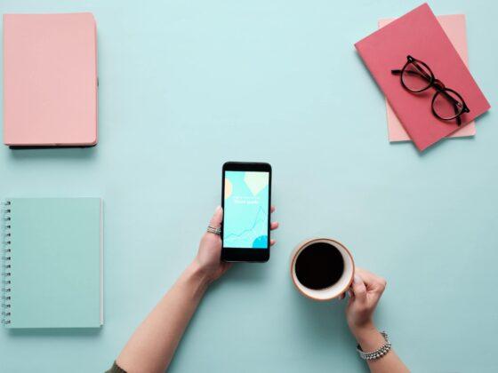 A phone, coffee, and notebooks in front of a light blue background.